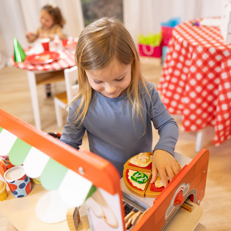 A kid playing with The Melissa & Doug Wooden Pizza Food Truck Activity Center with Play Food, for Boys and Girls 3+