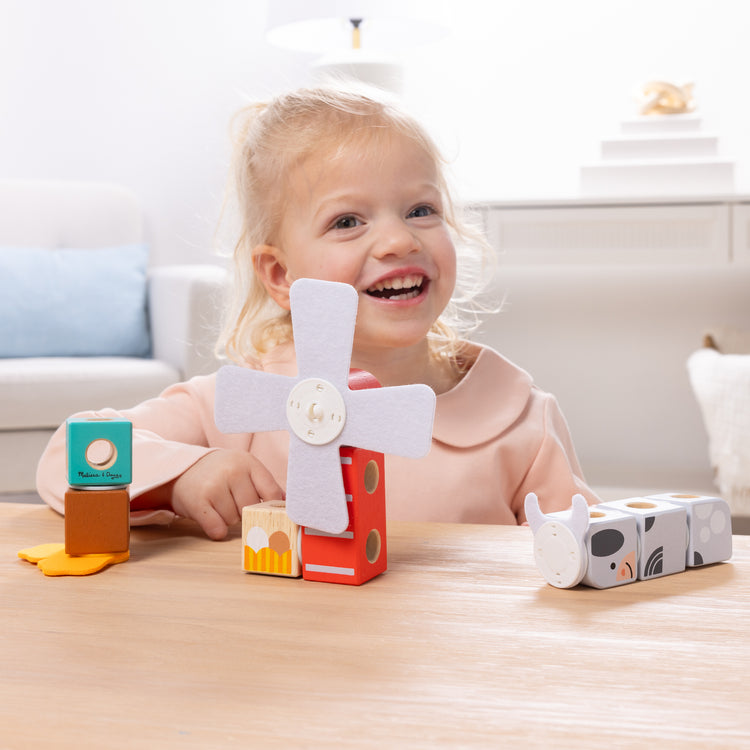 A kid playing with The Melissa & Doug Blockables™ Farm and Woodland 2-Pack Bundle Connectable Wooden Building Blocks Preschool Play Set Toy 