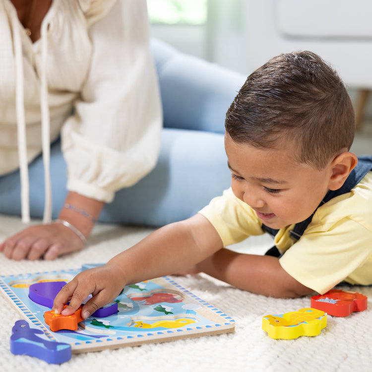 A kid playing with The Melissa & Doug Sea Creatures Ocean Wooden Chunky Puzzle - 7 Pieces