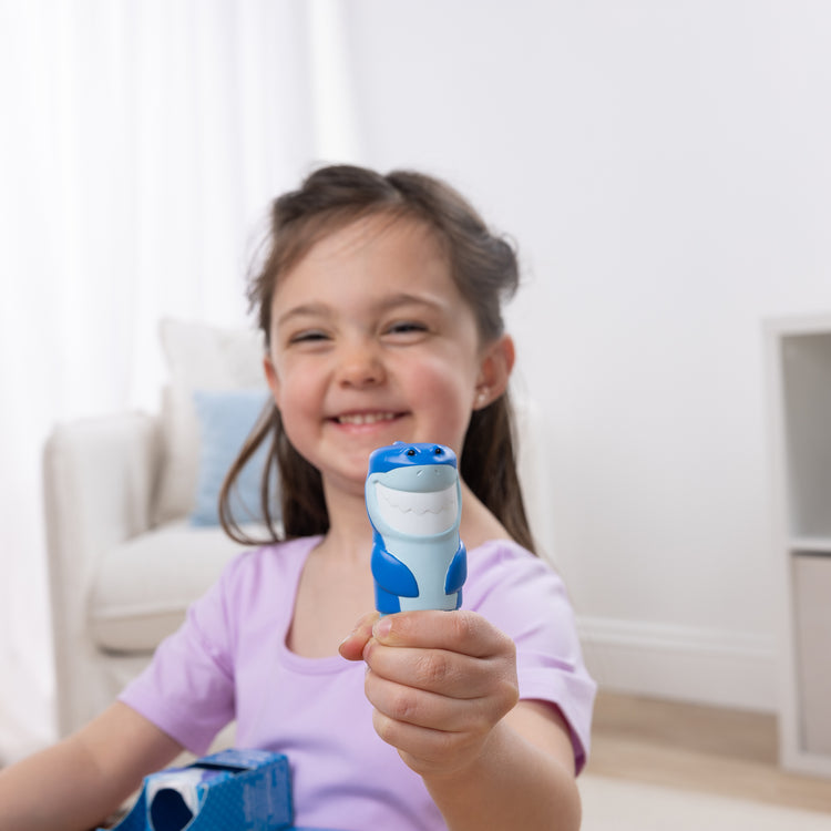 A kid playing with The Melissa & Doug Sticker WOW!™ Shark Bundle: 24-Page Activity Pad, Sticker Stamper, 500 Stickers, Mini Pad, Arts and Crafts Fidget Toy Collectible Character