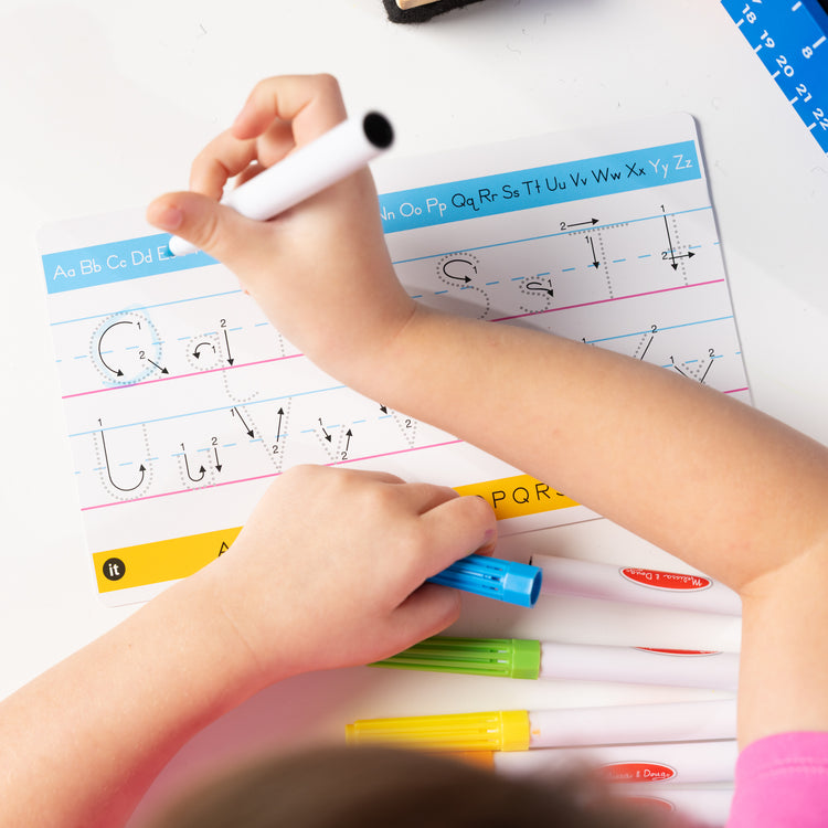 A kid playing with The Melissa & Doug Take-Along Double-Sided Wooden Tabletop Activity Art Easel; Portable Travel Toy with Whiteboard, Chalkboard, Arts and Crafts Accessories