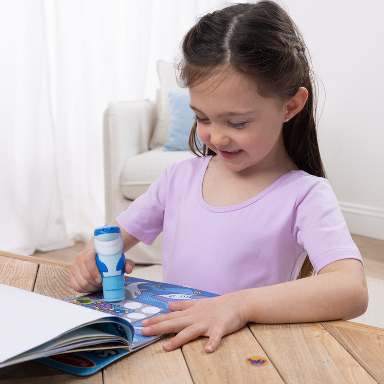 A kid playing with The Melissa & Doug Sticker WOW!™ 24-Page Activity Pad and Sticker Stamper, 300 Stickers, Arts and Crafts Fidget Toy Collectible Character – Shark