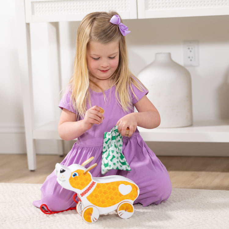 A kid playing with The Melissa & Doug Feed, Walk & Poo Pup Wooden Preschool Pull Toy Play Set Ages 3+