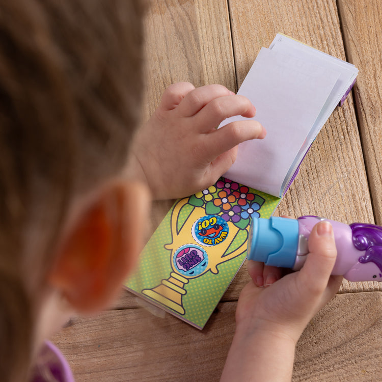 A kid playing with The Melissa & Doug Sticker WOW!™ Mini Activity Pad and 200+ Refill Stickers for Sticker Stamper Arts and Crafts Fidget Toy Collectibles – Assorted Way to Go! Reward Stickers