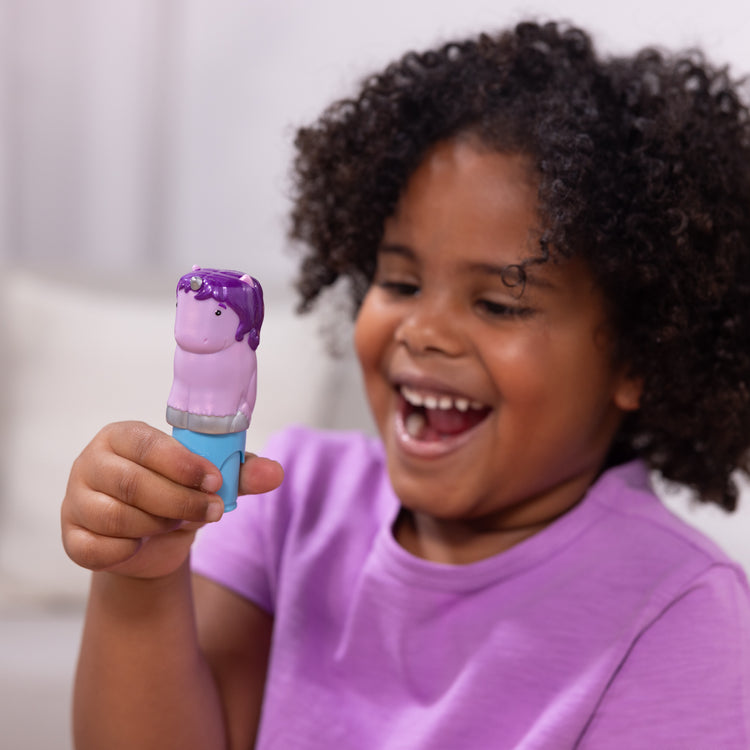 A kid playing with The Melissa & Doug Sticker WOW!™ 24-Page Activity Pad and Sticker Stamper, 300 Stickers, Arts and Crafts Fidget Toy Collectible Character – Sprinkles the Purple Unicorn