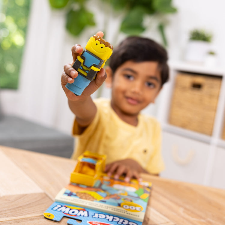 A kid playing with The Melissa & Doug Sticker WOW!™ Bulldozer Bundle: 24-Page Activity Pad, Sticker Stamper, 500 Stickers, Arts and Crafts Fidget Toy Collectible Character