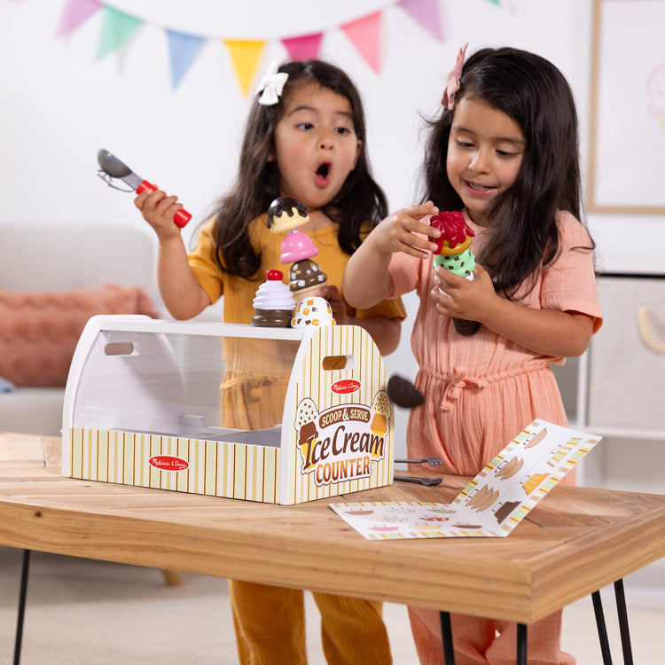 A kid playing with The Melissa & Doug Wooden Scoop and Serve Ice Cream Counter With Play Food and Accessories (28 Pcs) 
