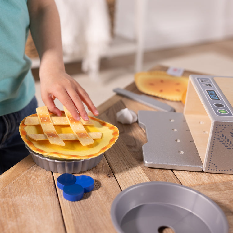 A kid playing with The Melissa & Doug Make and Bake Pies Pretend Play Food Set And Wooden Oven With Squishy Dough for Ages 3+