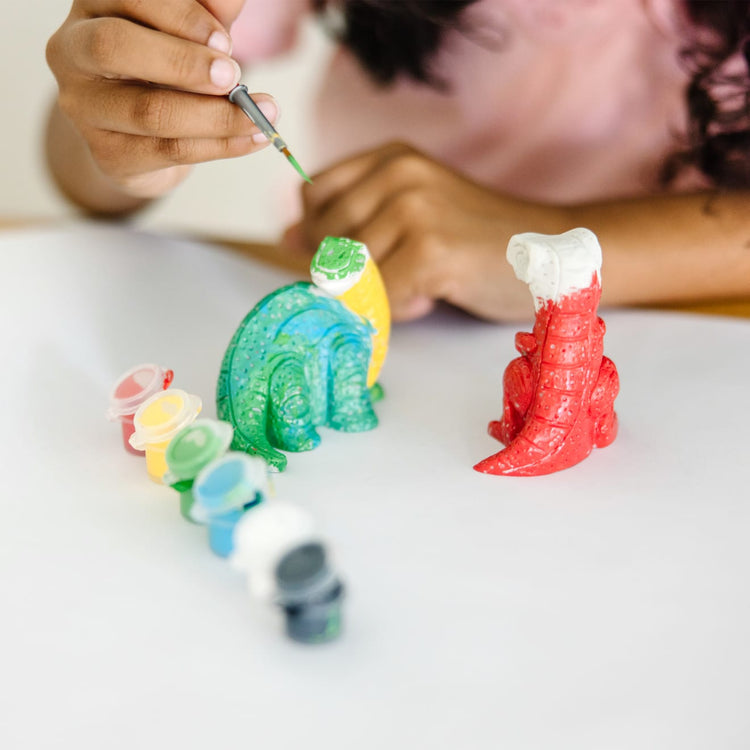 A kid playing with the Melissa & Doug Created by Me! Dinosaur Figurines Craft Kit (2 Resin Dinosaurs, 6 Paints, Paintbrush)