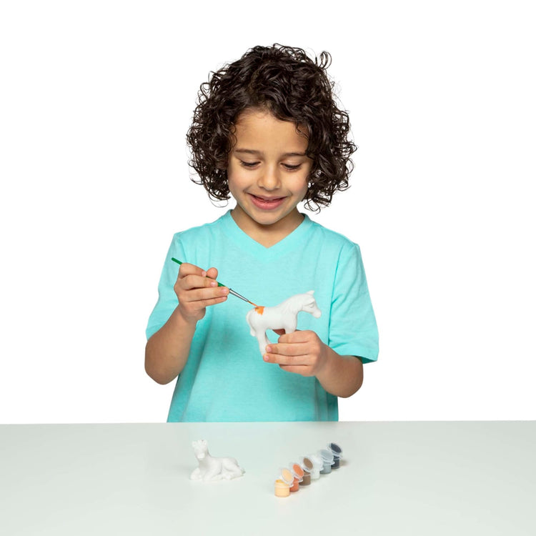 A child on white background with the Melissa & Doug Created by Me! Horse Figurines Craft Kit (2 Resin Horses, 6 Paints, Paintbrush)